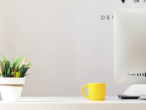 yellow ceramic mug beside gray aluminum iMac